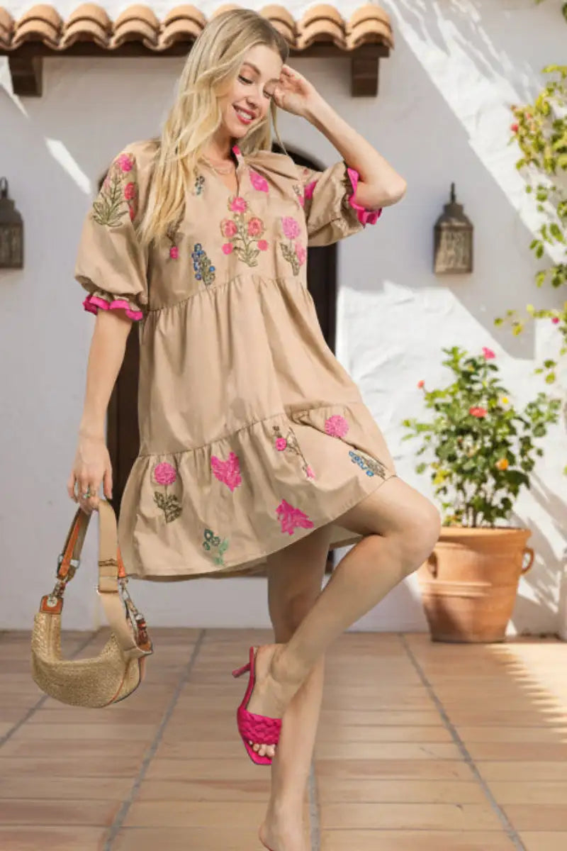 Beige floral-embroidered dress with pink ruffled sleeves and hem, featuring a tiered skirt design.